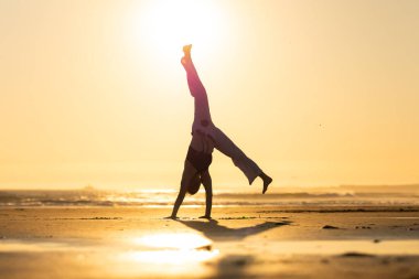 Kumlu bir plajda takla atan bir insan güzel bir altın gün batımında
