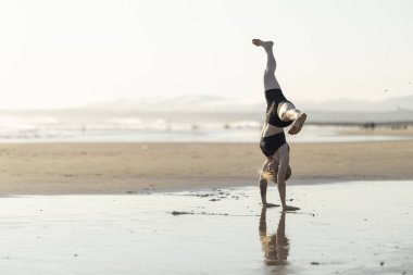 Gün batımında plaj antrenmanında baş aşağı duran genç bir kadın.