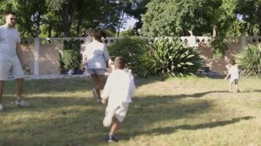 Aile güneşli bir günde parkta kovalamaca oynuyor.