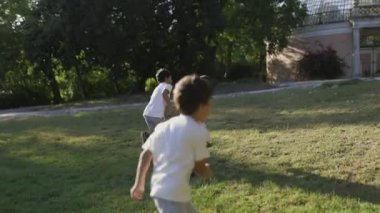 Parktaki bir cam evin yakınındaki çimenlikte koşup kovalamaca oynayan mutlu çocuklar.