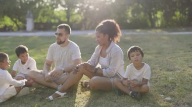 Aile birlikte güzel vakit geçiriyor, parkta çimenlerde oturuyor, hikayelerini paylaşıyor ve gülüyor.
