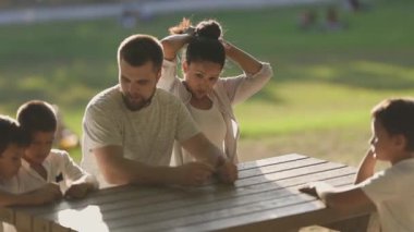 Ebeveynler ve çocuklar güneşli bir parkta eğleniyorlar, eğlenceli etkileşimler içindeler.