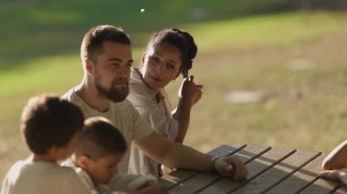 Mutlu aile, parkta piknik masasında birlikte vakit geçiriyor.