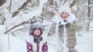Kış ormanı İki mutlu küçük kız yan yana durur ve kar fırlatırlar. Orta çekim