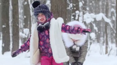 Kış ormanında karla oynayan iki küçük kız. Kızların yüzünde kar var. Orta çekim