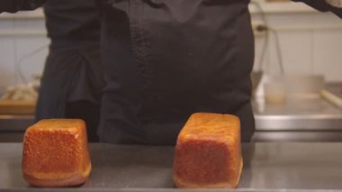 Profesyonel bir fırıncı metal bir tezgahın üzerine fırından taze ekmek çıkarıyor.