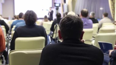 Konferans salonunda oturan insanlar, profesyonel bir seminer veya atölye sırasında sunum izliyorlar.
