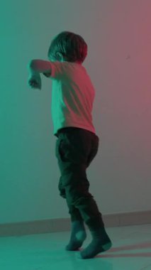 Enerjik bir çocuk, gök mavisi ve pembe ışıklarla aydınlatılmış bir odada doğaçlama dans ediyor.