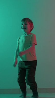 Enerjik çocuk, gök mavisi ve kırmızı sahne ışıkları altında çeşitli dans hareketleri yapar.