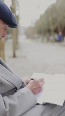 Kulaklık takan son sınıf öğrencisi bankta otururken deftere yazıyor.