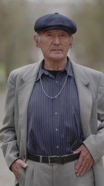 Parkta kıdemli bir adam duruyor, elleri cebinde.