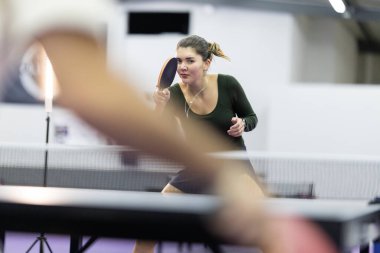 Masa tenisi oynayan genç bir kadın, konsantrasyonuyla oyuna odaklanıyor.