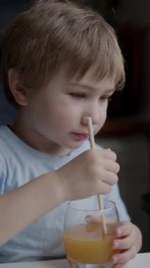 Anaokulu öğrencisi tabletten video izlerken tekrar kullanılabilir pipetle portakal suyu içiyor