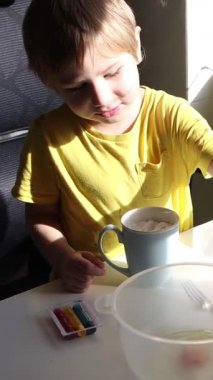 Çocuk kaseye çikolata tozu ekliyor, çikolatalı süt içeceği hazırlıyor.