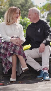 Alçak bir duvarda oturan olgun bir çift, güneşli madeira botanik bahçesinde mutlu bir şekilde sohbet ediyorlar.