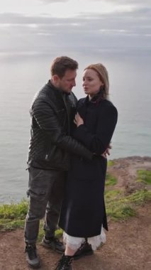 Çift gün batımında okyanusa bakan bir uçurumda romantik bir anın tadını çıkarıyor.