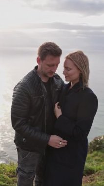 Gün batımında okyanusa bakan bir uçurumda öpüşen romantik çift.