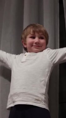 Enerjik çocuk perdelerin önünde özgürce dans ediyor, neşe ve hareket ifade ediyor.