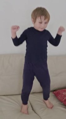 Küçük çocuk kanepede çıplak ayakla dans ediyor, evde eğleniyor.