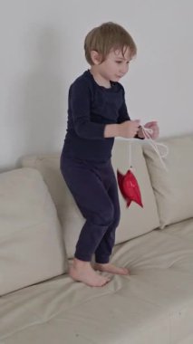 Sarışın çocuk beyaz bir kanepede kırmızı yıldız şeklinde bir balonla oynuyor.