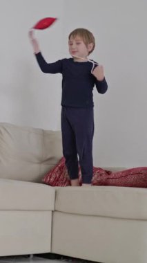 Sarışın bir çocuk kırmızı yıldız şeklinde bir balonla beyaz bir kanepede zıplayıp oynuyor.