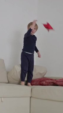 Mutlu çocuk kanepede zıplayıp kırmızı yıldız şekilli oyuncaklarla oynuyor.