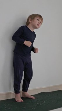 Küçük çocuk beyaz bir duvara karşı yoga minderinde dans ediyor.