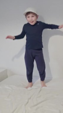 Mutlu çocuk beyzbol şapkası takıyor ve yatakta dans ediyor.