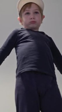 Beyaz şapkalı ve koyu renk elbiseli bir çocuk yatak odasında dans figürleri yapıyor.