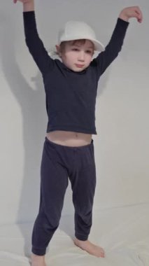 Enerjik çocuk yatak odasındaki yatakta dans figürleri yapıyor, beyzbol şapkası takıyor.