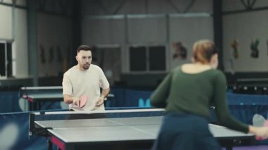Konsantre genç adam ve kadın bir spor kulübünde masa tenisi oynuyorlar.
