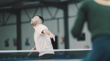 Genç adam rekabetçi bir ping-pong oyunu sırasında topa servis yapmaya ve vurmaya konsantre oluyor.