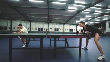 İki yetenekli sporcu, modern bir spor tesisinde masa tenisi oynuyorlar.