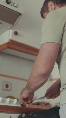 Evcil mutfakta ahşap tahtada malzemeleri kesen adam.