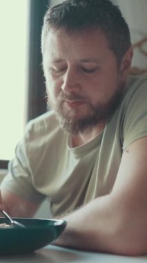 Sıradan bir yetişkin adam mutfağında kahvaltı gevreğinin tadını çıkarıyor.