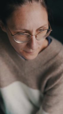 Gözlük takan ve günlük kıyafetler giyen kadın mutfaktaki bardaktan su içiyor.