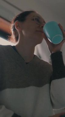 Bir kadın mutfağında çay ya da kahve içiyor.