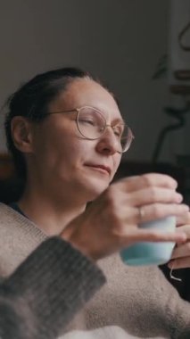 Mutfakta sıcak bir içecekten hoşlanan kadın, pencereden dışarı bakıyor.