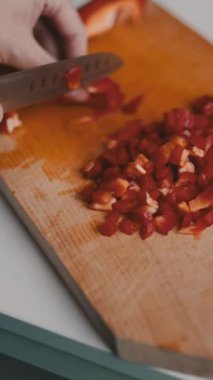 Şefin elleri ahşap bir kesme tahtasına kırmızı bir dolma biber keserken, yemek tarifi için malzemeleri hazırlarken yakın çekim.