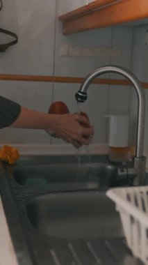 Ev hanımı mutfak lavabosunda akan suyun altında domates yıkıyor.