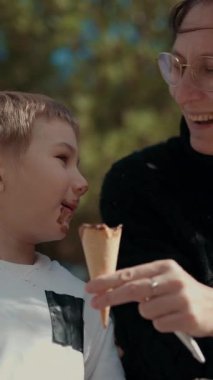 Anne ve oğlu parktaki bankta çikolatalı dondurmanın tadını çıkarıyorlar.