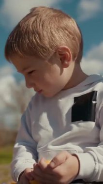 Güneşli bir günde dışarıda oturan çocuk muz soyar.