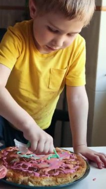 Çocuk renkli kremayla bir doğum günü pastasını dikkatlice dekore ediyor.