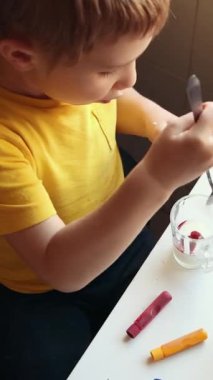 Anaokulu öğrencisi renkli balmumunu kaşıkla karıştırıyor.