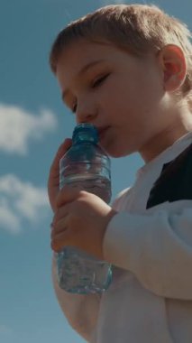 Güneşli bir günde plastik şişeden suyla su içen çocuk.