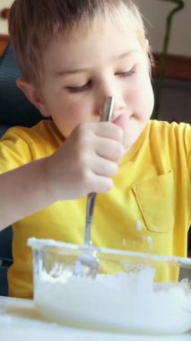 Genç bir çocuk cam bir kâseye beyaz malzemeleri karıştırıyor.