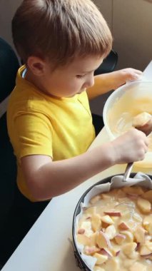 Genç çocuk dilimlenmiş elmaların üzerine dikkatlice hamur dökerek lezzetli bir elmalı turta hazırlıyor.