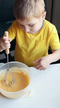 Beyaz bir masada kasedeki malzemeleri çırpan çocuk.