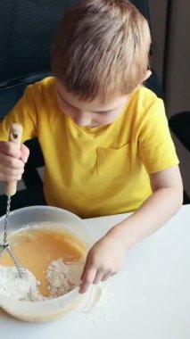 Çocuk yemek yapmayı öğreniyor. Malzemeleri beyaz bir masada karıştırıyor.