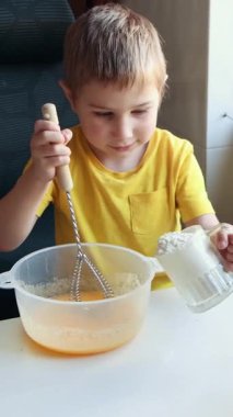 Çocuk dikkatli bir şekilde yemek yapmayı öğreniyor kaseye malzeme ekleyerek ve çırparak.